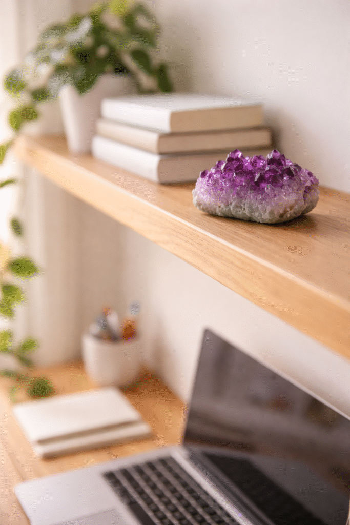  drusa de ametista em prateleira acima de mesa de home office com plantas e livros ao fundo