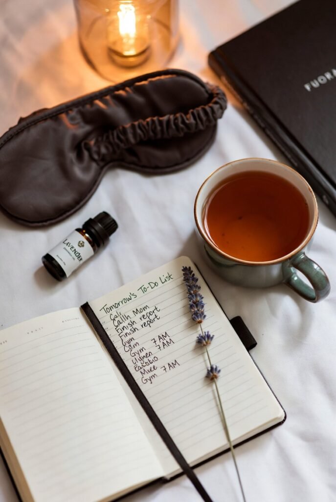 flat lay com diário aberto chá de ervas máscara de dormir óleo essencial de lavanda livro e flores secas iluminados por luz âmbar representando os elementos de uma rotina noturna eficaz para treinar o cérebro a associar esses gestos com o início do sono